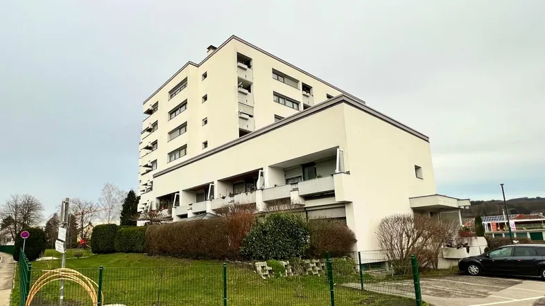 Modernes Mehrfamilienhaus mit mehreren Balkonen und gepflegter Grünanlage in städtischer Umgebung.