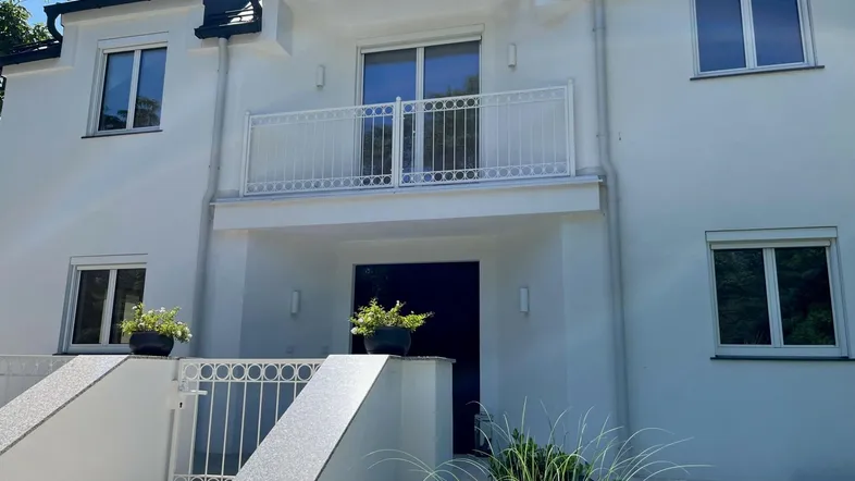 Moderne weiße Fassade eines Reihenhauses mit Balkon und gepflegtem Eingangsbereich.