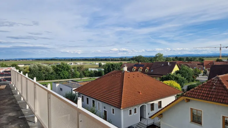 Weitläufiger Blick über eine ländliche Wohngegend mit Feldern und Häusern unter blauem Himmel.
