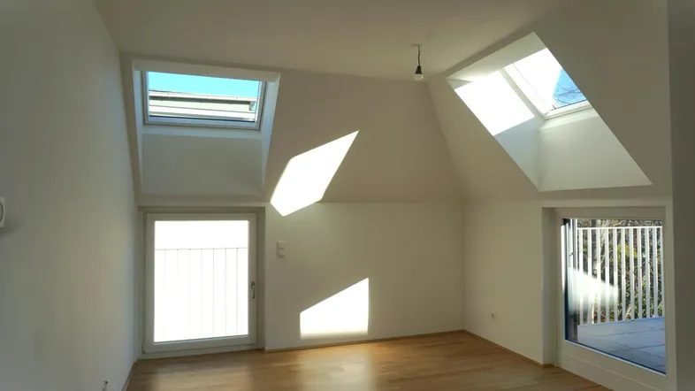 Heller Dachgeschossraum mit schrägen Decken, zwei Dachfenstern und Zugang zum Balkon.
