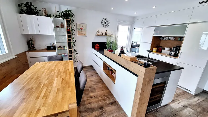 Helle, moderne Küche mit weißen Schränken, Kochinsel und Essbereich mit Holztisch und Bank.