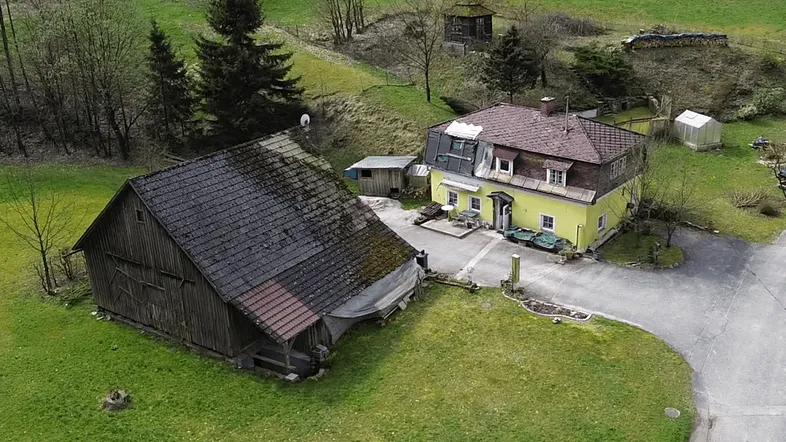 Luftaufnahme eines gelben Hauses und einer Scheune in einer grünen, ländlichen Umgebung.