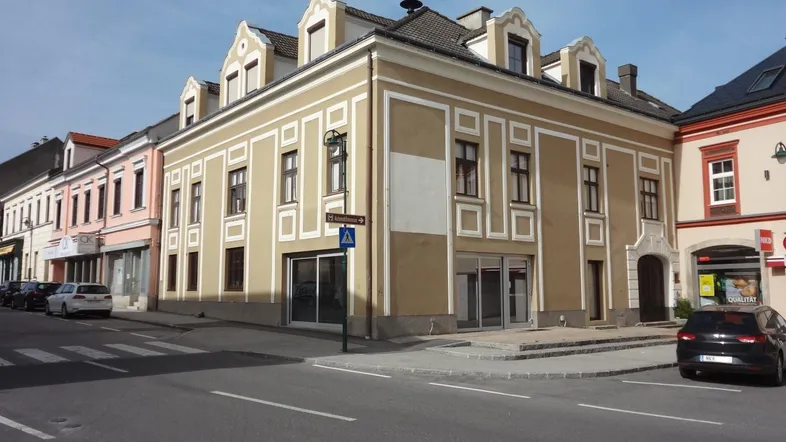 Historisches Eckgebäude an einer belebten Straße mit großen Schaufenstern im Erdgeschoss und traditionellen Details.