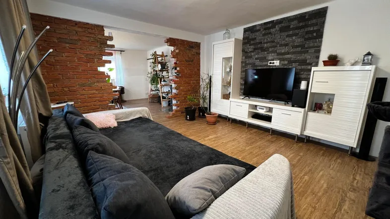 Gemütliches Wohnzimmer mit dunklem Sofa, Holzboden und dekorativer Ziegelwand.