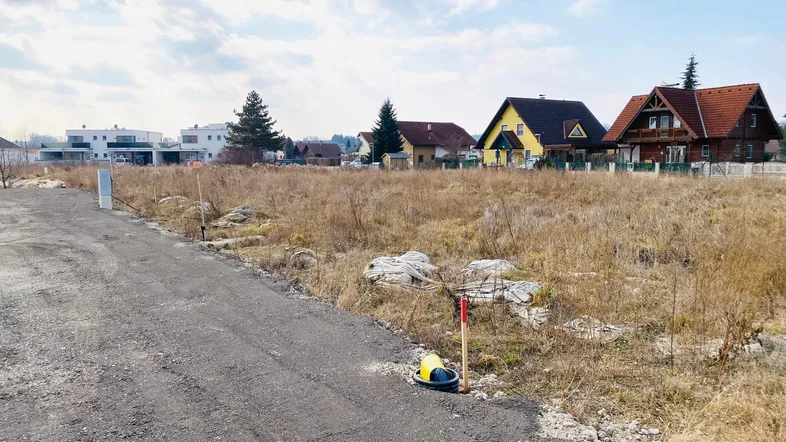 Ungenutztes Grundstück mit trockenem Gras und Häusern im Hintergrund, bereit für die Bebauung.