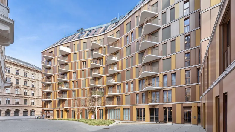 Moderne Wohnanlage mit geschwungener Fassade und zahlreichen Balkonen in urbaner Umgebung.