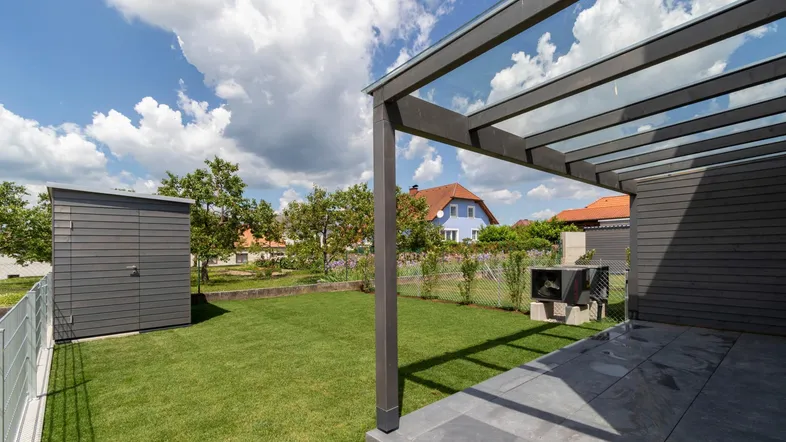 Großer Gartenbereich mit Rasenfläche, Gartenhaus und überdachter Terrasse, ideal für Entspannung im Freien.