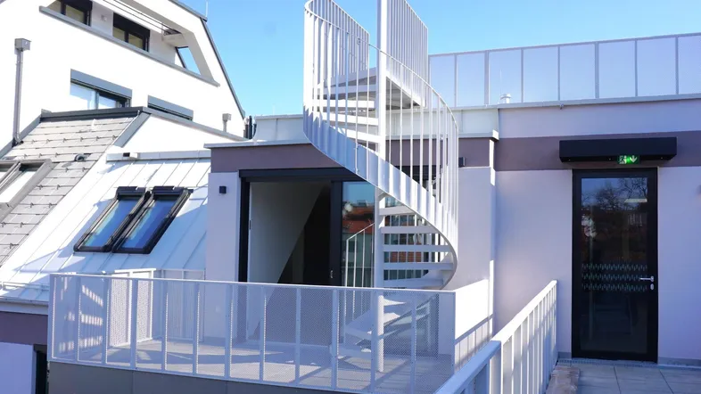Heller Balkon mit moderner Wendeltreppe, die zu einer weiteren Dachterrasse führt, umgeben von Wohngebäuden.