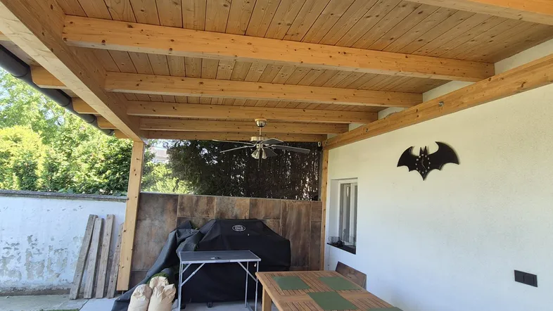 Überdachte Terrasse mit Holzbalken, Essbereich und Grill, ideal für gesellige Stunden im Freien.