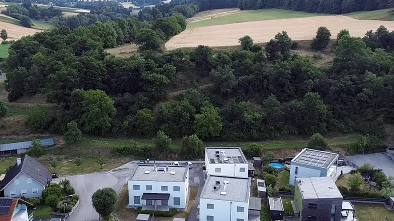 Weitläufige Luftaufnahme der modernen Reihenhäuser eingebettet in eine grüne Hügellandschaft.