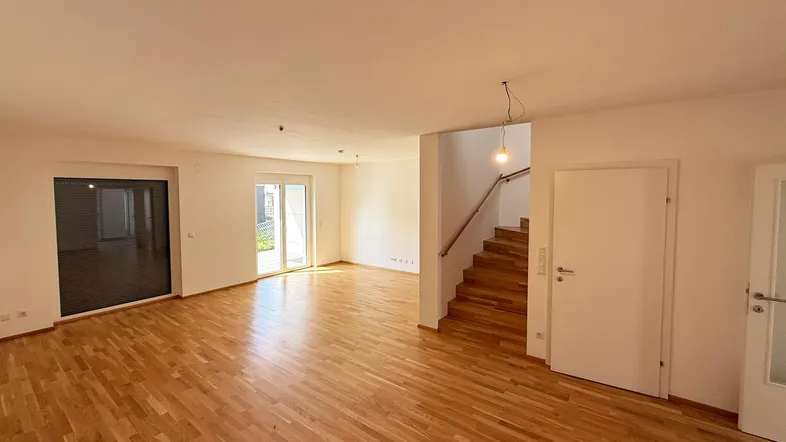 Helles, leeres Wohnzimmer mit Eichenparkettboden, weißen Wänden und Zugang zur Terrasse.