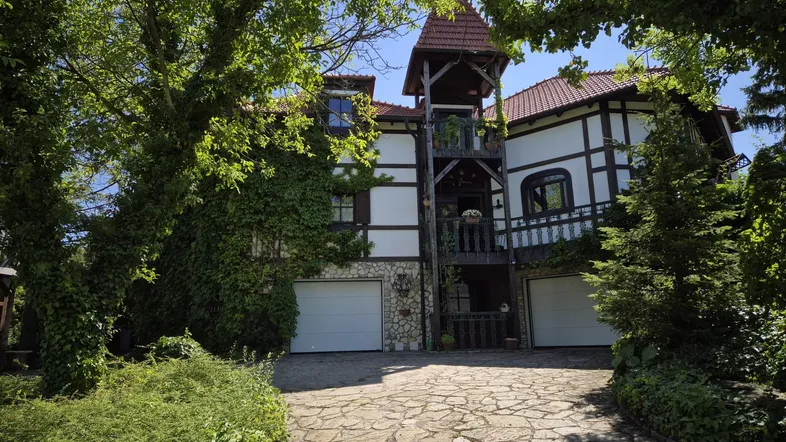 Traditionelles Fachwerkhaus mit zwei Garagen und begrüntem Eingangsbereich unter blauem Himmel.