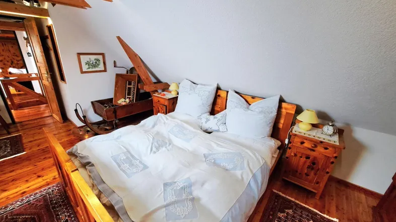 Gemütliches Schlafzimmer im Dachgeschoss mit Holzbalken, Holzboden und traditionellen Möbeln.