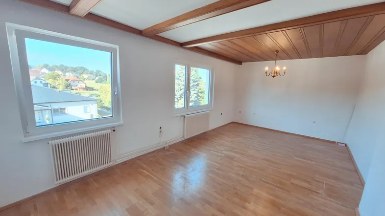 Geräumiges Wohnzimmer mit Holzbalkendecke, Parkettboden und Blick ins Grüne.