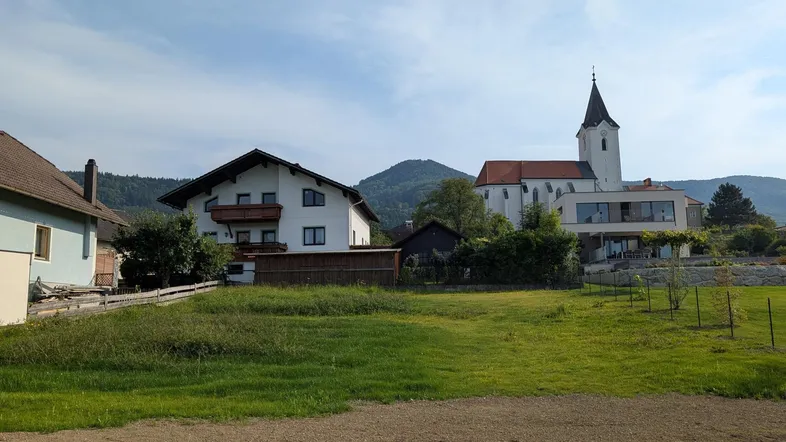 Grundstück in ländlicher Umgebung mit Blick auf eine Kirche, Berge und weitere Wohnhäuser.