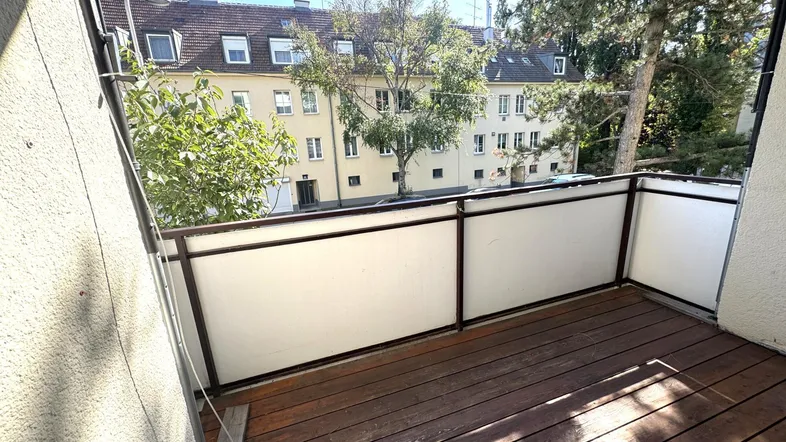 Geräumiger Balkon mit Holzboden und Blick auf die umliegenden Gebäude und Bäume.