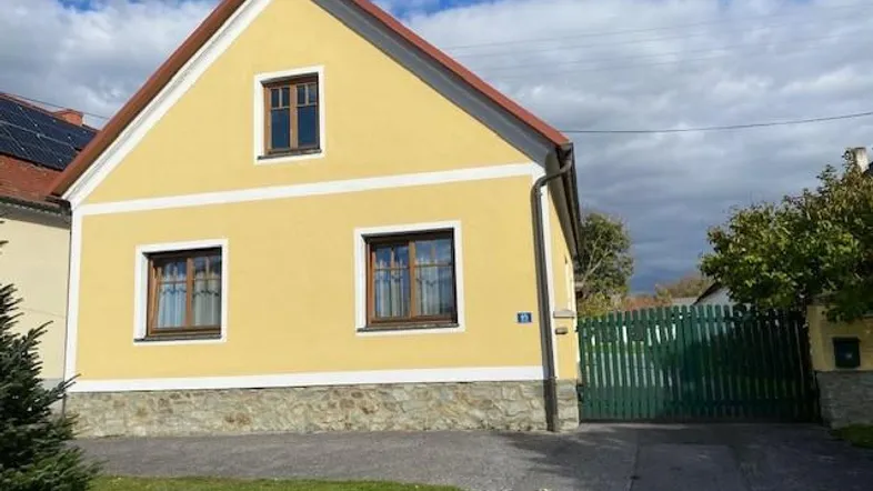 Gelbes Einfamilienhaus mit rotem Satteldach, braunen Fenstern und Steinsockel.