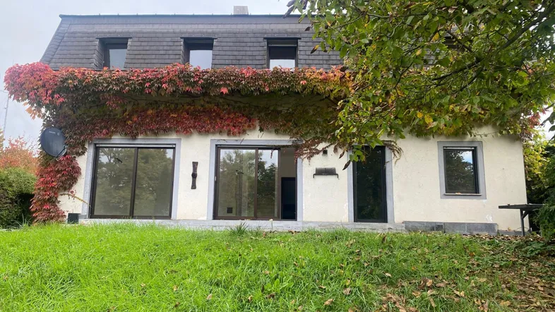 Hausfassade mit rotem Efeu bewachsen, großen Fenstern und Mansarddach.