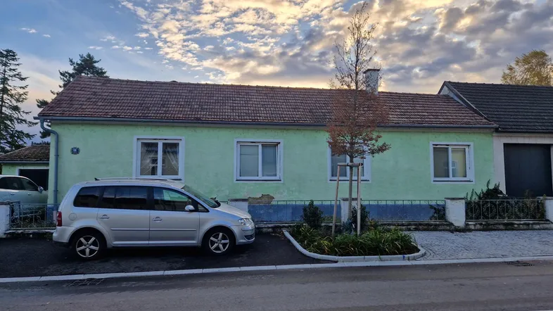 Vorderansicht eines älteren Hauses mit hellgrüner Fassade und einem geparkten Auto davor.