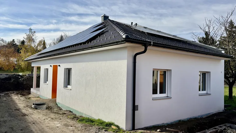 Neubau-Einfamilienhaus mit weißer Fassade, dunklem Dach und Photovoltaikanlage unter blauem Himmel.