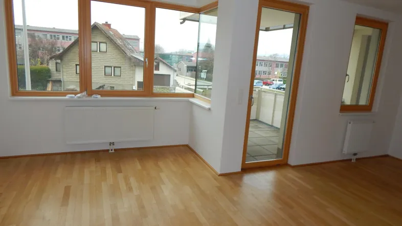 Helles Zimmer mit Holzparkettboden, großen Fenstern und Zugang zum Balkon.