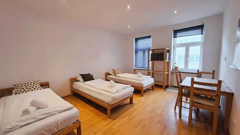 Geräumiges Zimmer mit drei Einzelbetten, Holzboden und einem Essbereich am Fenster.