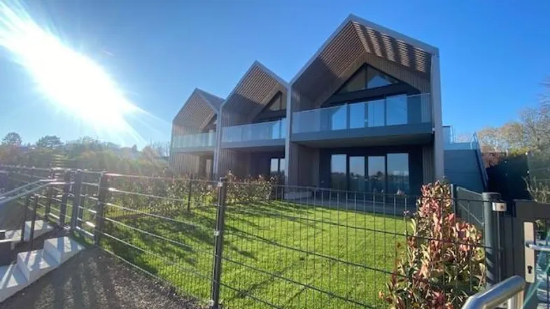Moderne Reihenhäuser mit markanten Giebeldächern und privatem Gartenbereich unter strahlendem Himmel.