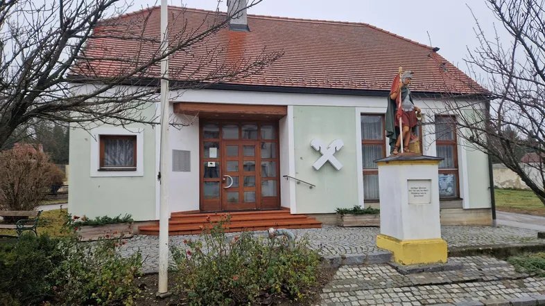 Traditionelles Gebäude mit hellgrüner Fassade, rotem Ziegeldach und einer Statue davor.