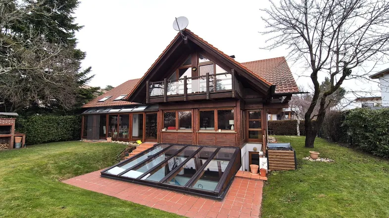 Großzügiger Gartenbereich mit Holzhausfassade, integriertem Poolzugang und gemauertem Grillplatz.