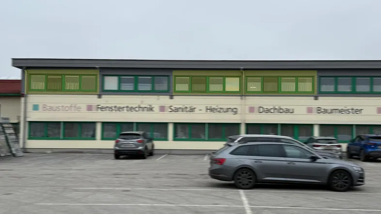 Moderne Außenansicht eines Geschäftsgebäudes mit grünen Fensterrahmen und einem weitläufigen Parkplatz davor.