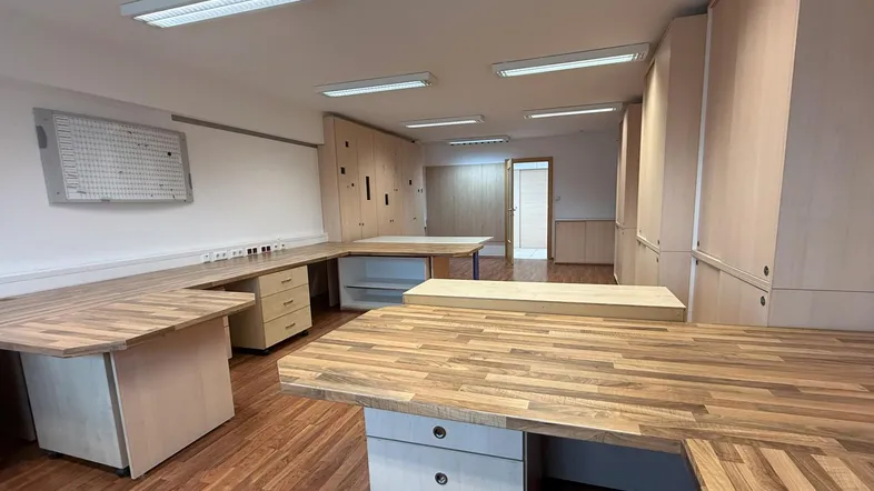 Geräumiges Büro mit mehreren Arbeitsplätzen, Holzoptik-Böden und hellen Einbauschränken, ideal für Teamarbeit.