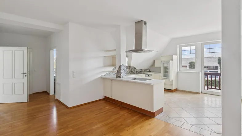 Heller offener Wohn-Essbereich mit Holzboden, integrierter Küche und Zugang zu einem kleinen Balkon.