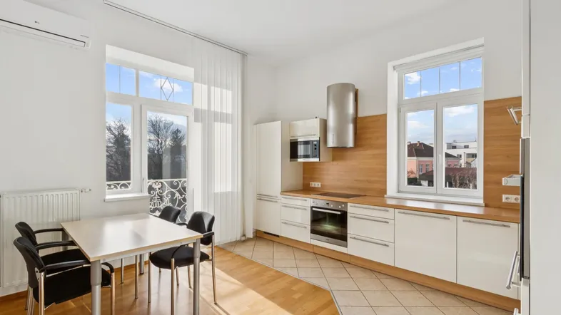 Moderne Einbauküche mit Essbereich, Holzakzenten und Fliesenboden. Helle Fenster lassen viel Licht herein.