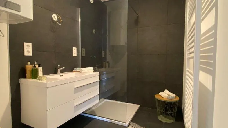 Modernes Badezimmer mit dunklen Fliesen, schwebendem Waschtisch und begehbarer Dusche.