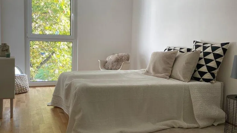 Helles Schlafzimmer mit Parkettboden, großem Fenster und Blick ins Grüne.