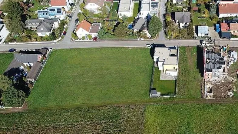 Luftaufnahme eines Baugrundstücks mit angrenzenden Wohnhäusern und einer Straße.