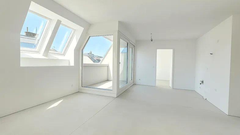 Lichtdurchfluteter Wohnraum im Dachgeschoss mit großen Dachfenstern und Balkonzugang.