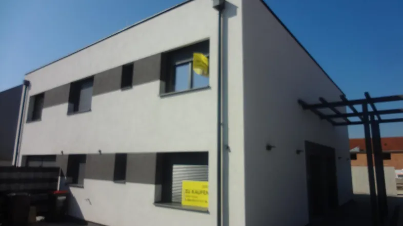 Modernes Gebäude mit weißer Fassade, dunklen Fenstern und einer Pergola im Außenbereich.