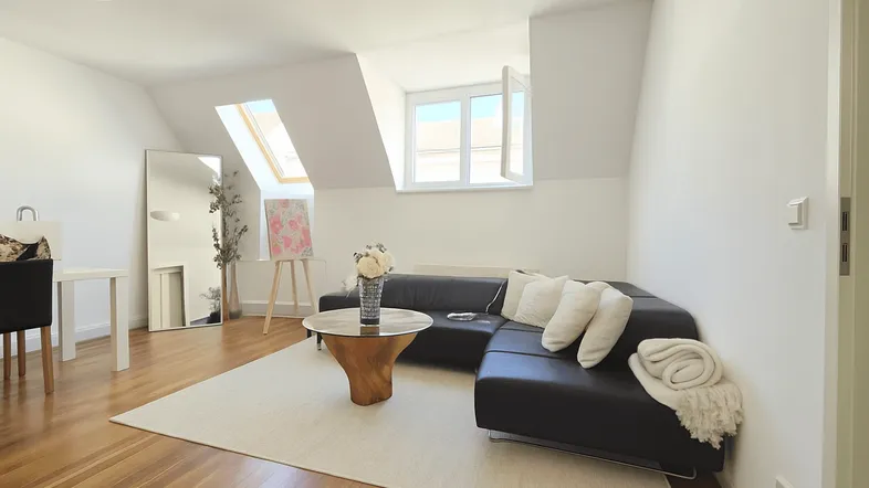 Helles Wohnzimmer im Dachgeschoss mit Holzboden, gemütlichem Sofa und Dachfenstern.
