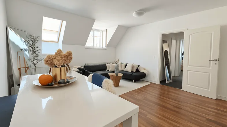 Geräumiges Wohnzimmer mit Holzboden, bequemer Sitzecke und viel Tageslicht durch Dachfenster.