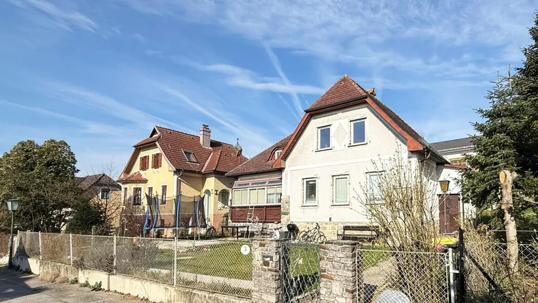 Ansicht des Hauses von der Straße mit Vorgarten und Nachbargebäuden unter blauem Himmel.