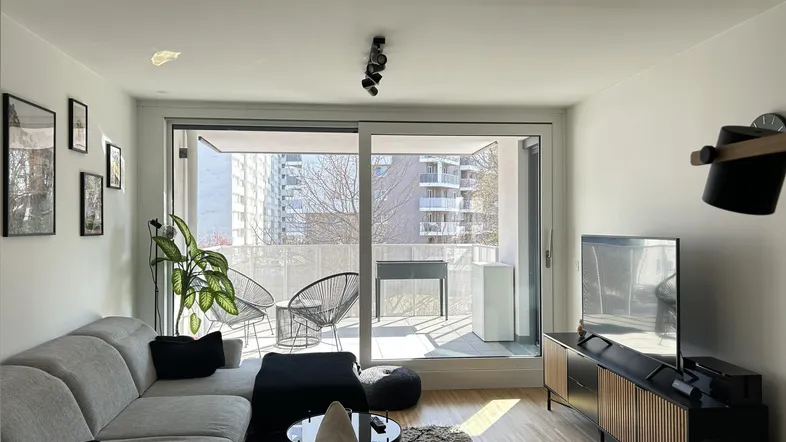 Helles Wohnzimmer mit Sofa, Holzboden und Zugang zu einem sonnigen Balkon.