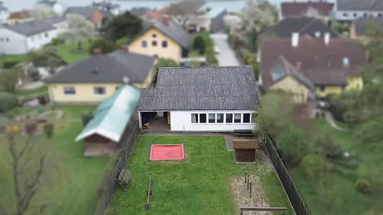 Rückansicht des Hauses mit großem Garten, Sandkasten und verschiedenen Spielgeräten für Kinder.