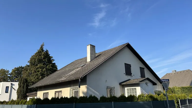 Traditionelles Haus mit Satteldach und weißer Fassade unter klarem blauem Himmel.