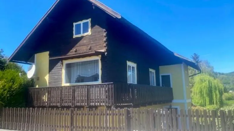 Traditionelles Haus mit Holzbalkon und gelber Fassade unter blauem Himmel.