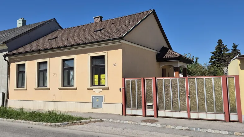 Vorderansicht des Hauses von der Straße aus mit gelber Fassade und braunem Dach an einem sonnigen Tag.
