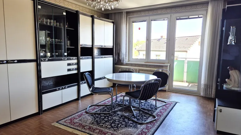 Geräumiges Wohnzimmer mit Parkettboden, großen Schränken und Zugang zu einem kleinen Balkon.