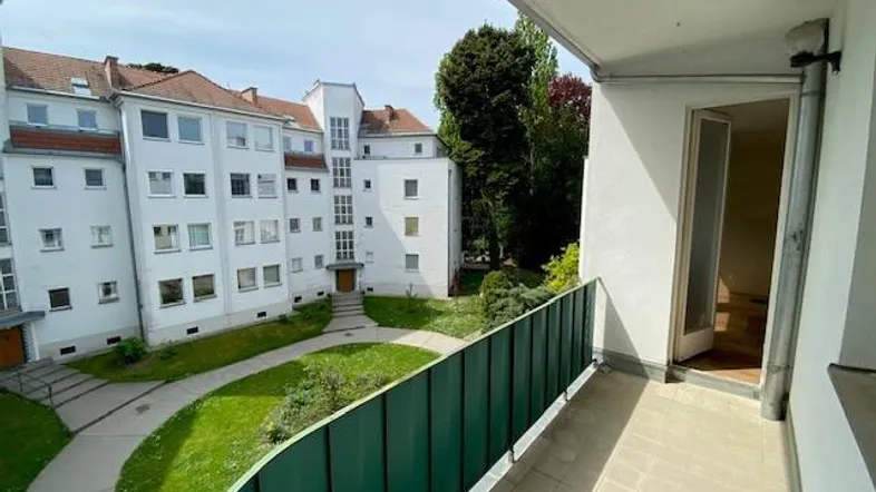 Geräumiger Balkon mit Blick auf den begrünten Innenhof und die umliegenden Gebäude der Wohnanlage.