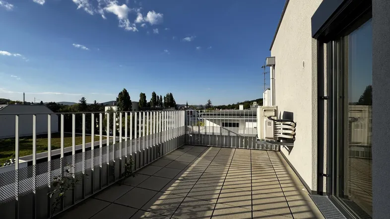 Geräumiger Balkon mit Fliesenboden und weitem Blick über die Umgebung unter blauem Himmel.