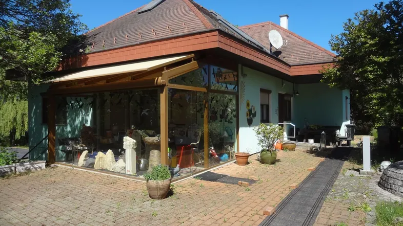 Seitenansicht des Hauses mit einem verglasten Wintergarten und einer gepflasterten Terrasse.